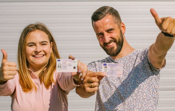 Du žmonės laiko vairuotojo pažymėjimus ir rodo nykščius į viršų.