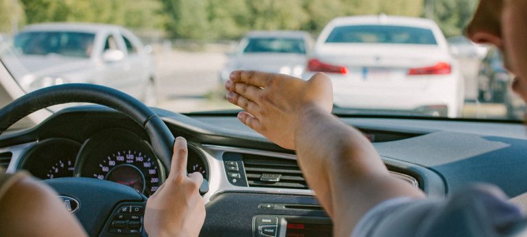 Vairavimo egzaminas automobilyje, egzaminuotojas ranka rodo kryptį